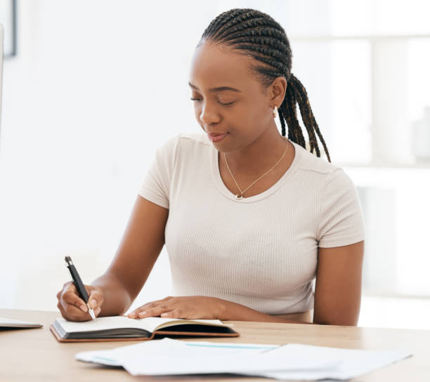 istock Notebook, working and black woman writing notes in office, sitting at desk. Ideas, vision and businesswoman with pen in hand to write, jot and taking notes in business meeting in book or work diary 1798792566