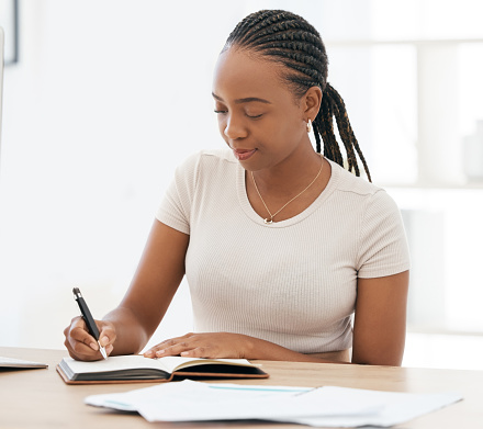 Notebook, working and black woman writing notes in office, sitting at desk. Ideas, vision and businesswoman with pen in hand to write, jot and taking notes in business meeting in book or work diary