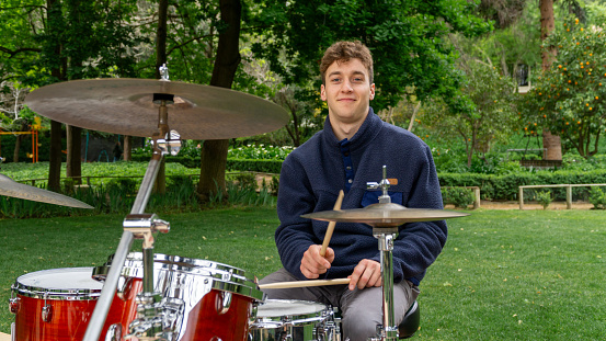 Young man smiling at the camera while practicing drums in his garden.
