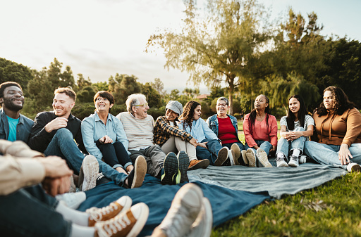 Happy multi generational people having fun sitting on grass in a public park - Diversity and friendship concept