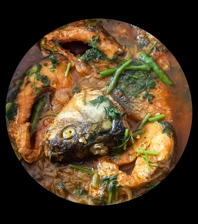 Ruhu rui or Katla Fish curry, traditional bangali fish curry with fresh green chilly and curry leaves on a grey textured background.