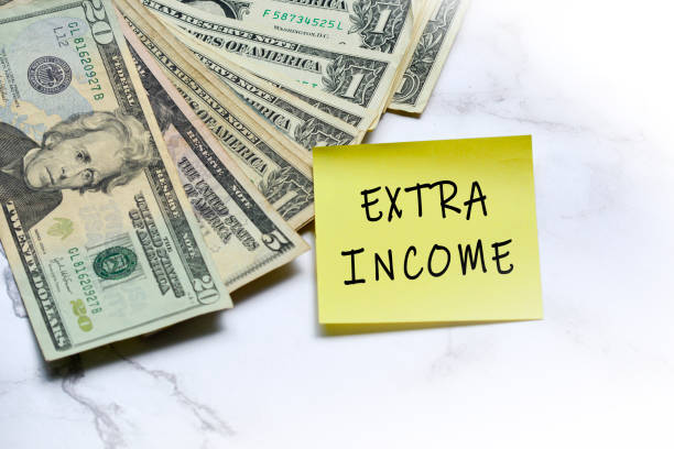 istock Dollars bill and stick note with text written EXTRA INCOME on mable table. 1798839266