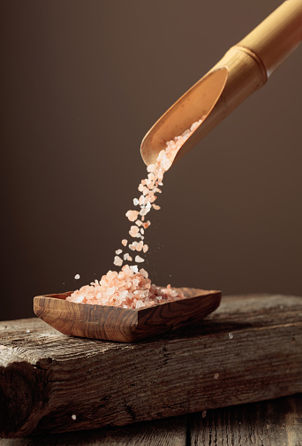 Pink salt is poured with a wooden spoon in the wooden dish. Copy space.