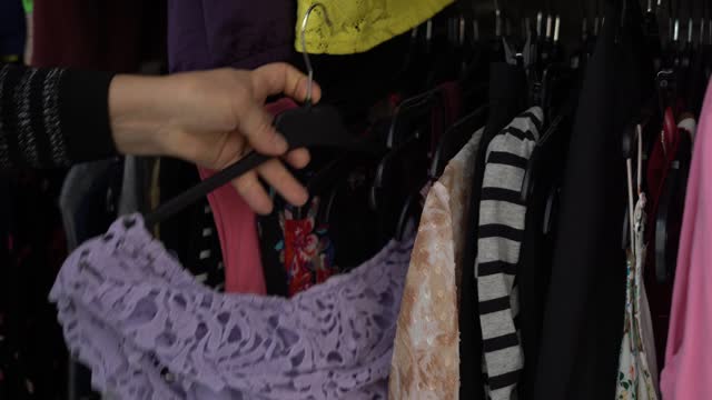Woman Buying Used Sustainable Clothes From Second Hand Charity Shop, Looking at lilac T-shirt