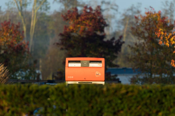 Biddinghuizen, Netherlands - 11 16 2023: An orange street mailbox of the Dutch postal company Postnl at the Spar convenience store on the grounds of Molecaten Park Flevostrand and Landal Waterparc Veluwemeer in the early November sun.