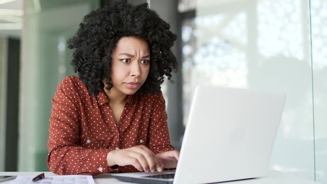 Frustrated young african american female complains about poor performance of software on laptop while sitting in office.