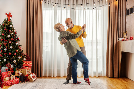 A playful and fun senior couple in love is dancing at home on christmas and new year.