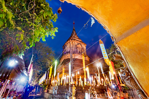 framed by pink blossom on trees,housing royal ashes of several Kings,illuminated by lights at dusk,alongside main north perimeter road of the Old historic Chiangmai City area.