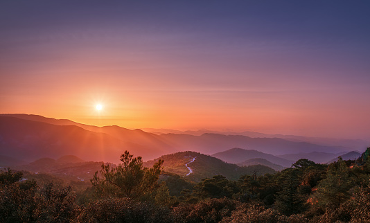 The rays of the setting sun illuminate the mountains and the trail leading through them. Horizontal photo.