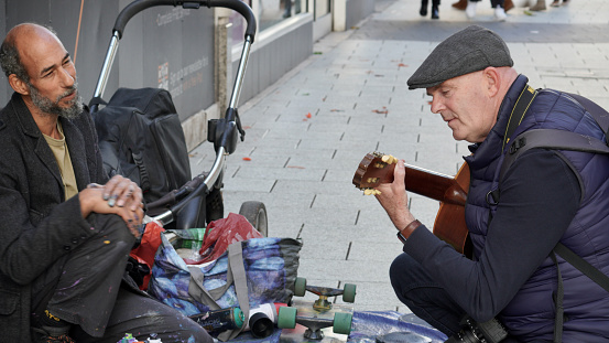 Cardiff, Wales, Oct 29 2023:  A street artist, fingers caked in spray paint, chats with a street photographer who plays the guitar he uses for busking, enjoy each others company and forge a friendship