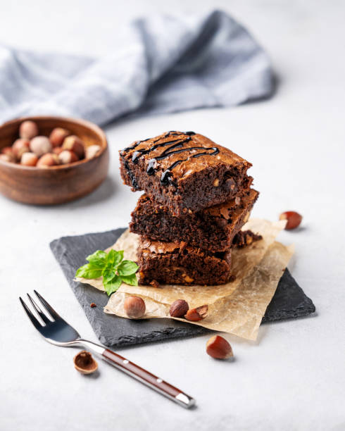 istock A stack of chocolate brownies with mint, hazelnuts and salted caramel on baking paper on a light background with fork and bowl with nuts. 1798972356