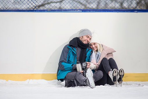 Happy Caucasian Couple in Winter With Ice Skates Skating and Having Fun While Drinking Tea Together on Ice Outdoors. Horizontal image