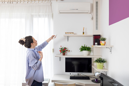 Woman turning on air conditioner. Crisis and inflation concept