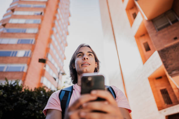 Young man looking around and using mobile phone outdoors
