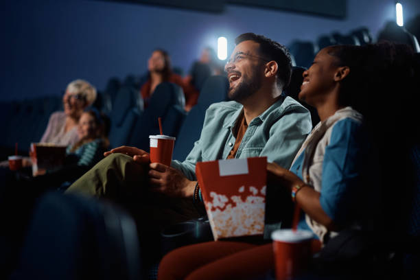 Young couple laughing while watching comedy movie in cinema.