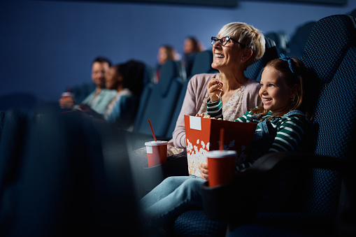 Happy little girl and her grandmother enjoying in movie projection in cinema.