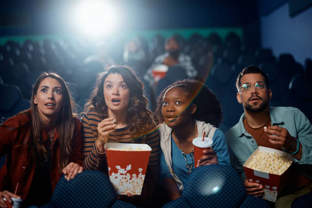 Multiracial group of friends watching suspenseful movie in theater. Amazed group of friends enjoying in movie projection in cinema. suspenseful stock pictures, royalty-free photos & images