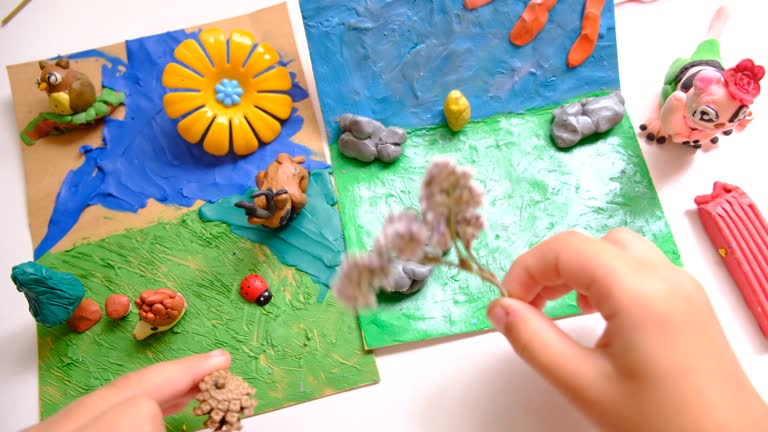 Child smearing colorful plasticine on cardboard and creating fairy tale card with cartoon animals, using nature details, dry flowers, cone, leaves