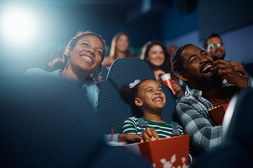 Cheerful African American family having fun while watching movie in a theater.