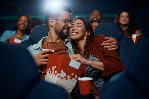 Young affectionate couple watching a movie on a date in cinema.