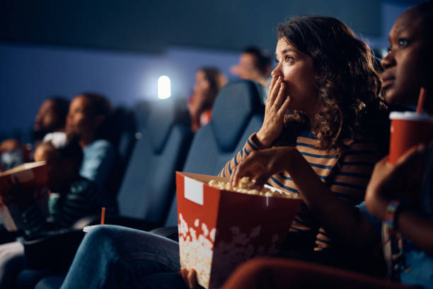 Shocked woman watching suspenseful movie in theater. Fearful woman while watching drama movie in cinema. suspenseful stock pictures, royalty-free photos & images