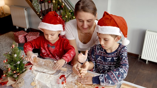 Young mother teaching her sons making traditional Christmas cookies on kitchen. Winter holidays, celebrations and party