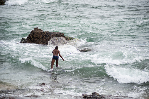Salvador, Bahia, Brazil - January 29, 2022: Fisherman is seen throwing fishing net on Rio Vermelho beach in the city of Salvador, Bahia.