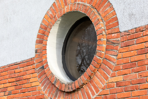 Round window. Red brick wall and light plaster.