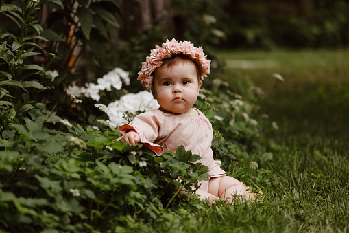 A beautiful baby girl, seven months old, sitting in a garden.