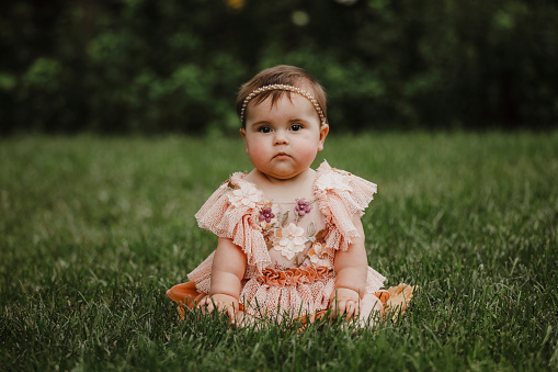 A beautiful baby girl, seven months old, sitting in a garden.