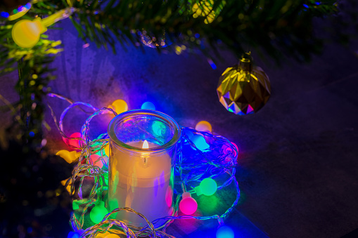 Cristmas candles with colorful Christmas lights, under branches of Christmas tree