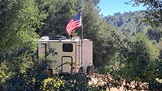 RV camper in wooded area with American flag