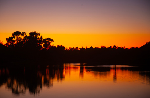 Lake near a forest area at sunset with bright orange sky