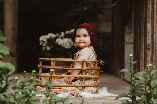 A beautiful baby girl, seven months old, sitting in a basket on a rustic porch.