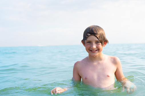 smiling boy swims in the sea in cloudy weather. happy child in the water, going to swim