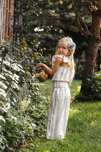A beautiful little girl, four years old, watering flowers in a garden.