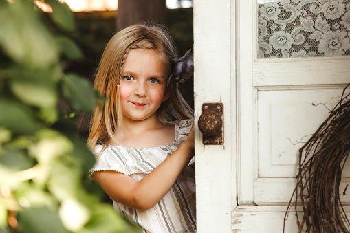 A beautiful little girl, four years old, peeks from behind a rustic door in a garden.