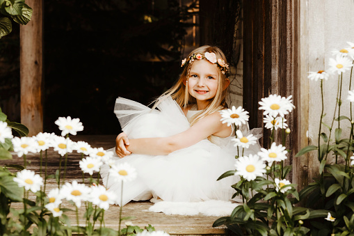 A beautiful little girl, four years old, smiles at the camera as she sits on a porch in a garden.