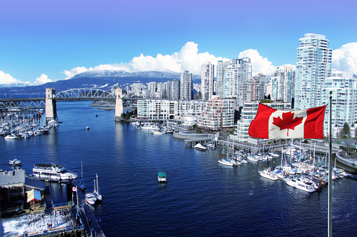 Canadian flag in front of the view of False Creek and the Burrard Street Bridge in Vancouver, Canada.