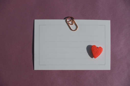 top view of red candy heart on a blank white gift card on pink shiny textured background, love valentine, communication and birthday celebration concept