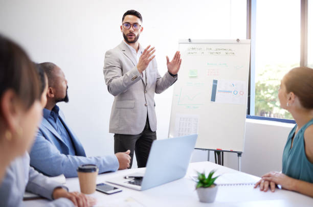 istock Presentation whiteboard, business people meeting and man speech, report or teaching group, team or workshop. Strategy, management and corporate speaker explain project to listening professional staff 1799304877