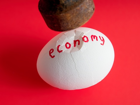 Impact, the pressure on the economy as the egg begins to crack. A concept of a broken economy using an egg and hammer on red background.