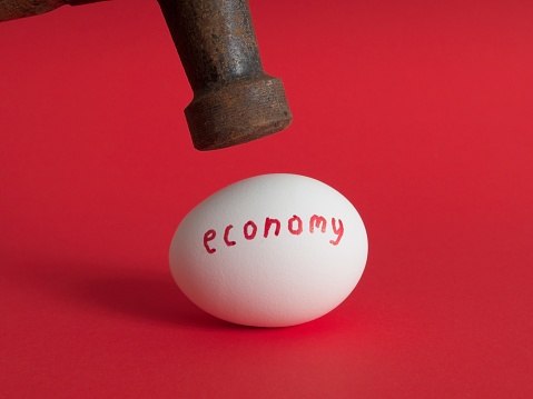 The fragile economy about to be crushed. A concept image of hammer about to impact a fragile egg representing the economy.