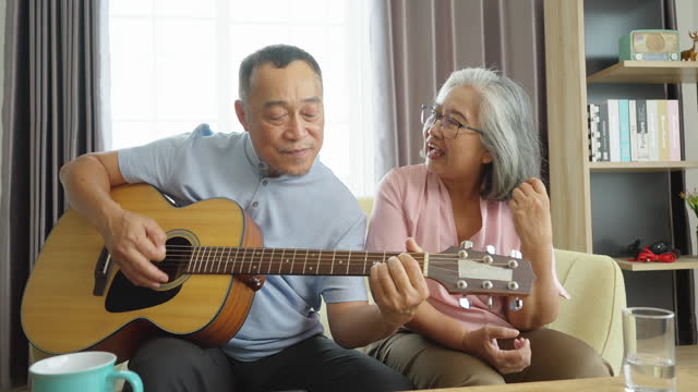 A joyful senior couple playing acoustic guitar and singing at home.