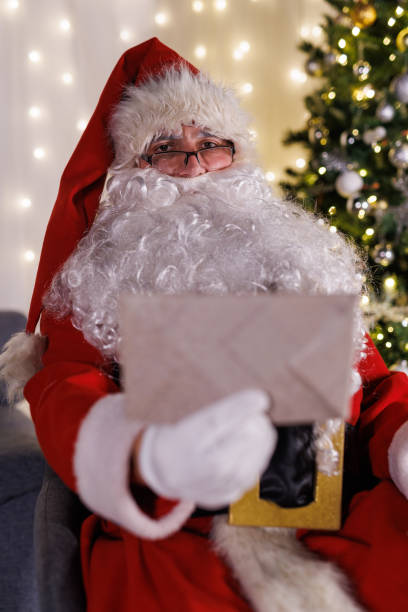 istock Santa sitting by the Christmas tree, reading letters from kids 1799373795