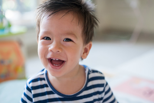 Portrait of a happy smiling adorable baby boy. His eyes are smiling and shining, and his smile reveals small teeth that are just growing. He is wearing a striped t-shirt