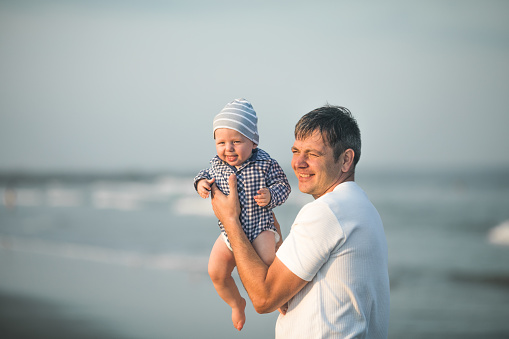 Happy Fathers day. Father and baby play on the beach. Dad and him Child together enjoying sunset. Loving single father hugs cute little son.