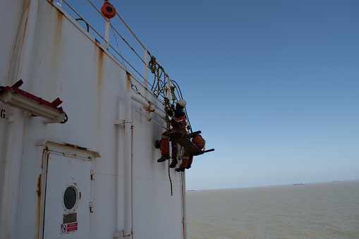 Sao luis anchorage, on board ship - november 14, 2023 : crew members of a cargo ship painting on the accomodation bulkhead sitting of a fallen chair arrangement