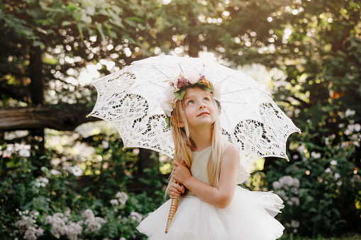 A beautiful little girl, four years old, smiling as she stands  in a garden under a vintage parasol.