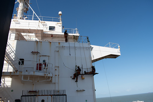 Sao luis anchorage, on board ship - november 14, 2023 : crew members of a cargo ship painting on the accomodation bulkhead sitting of a fallen chair arrangement